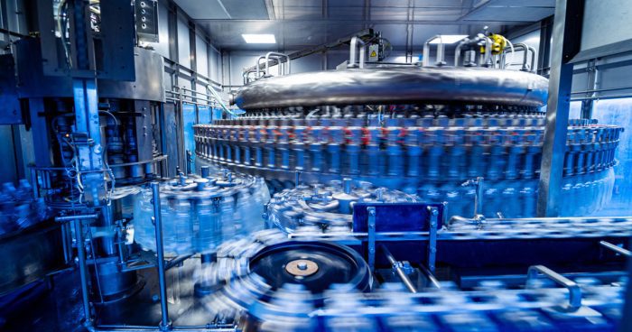 Automatic filling machine pours water into plastic PET bottles at modern beverage plant Credit: romaseti, iStock